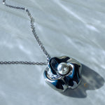Silver pendant necklace with pearl reflecting natural light on satin surface