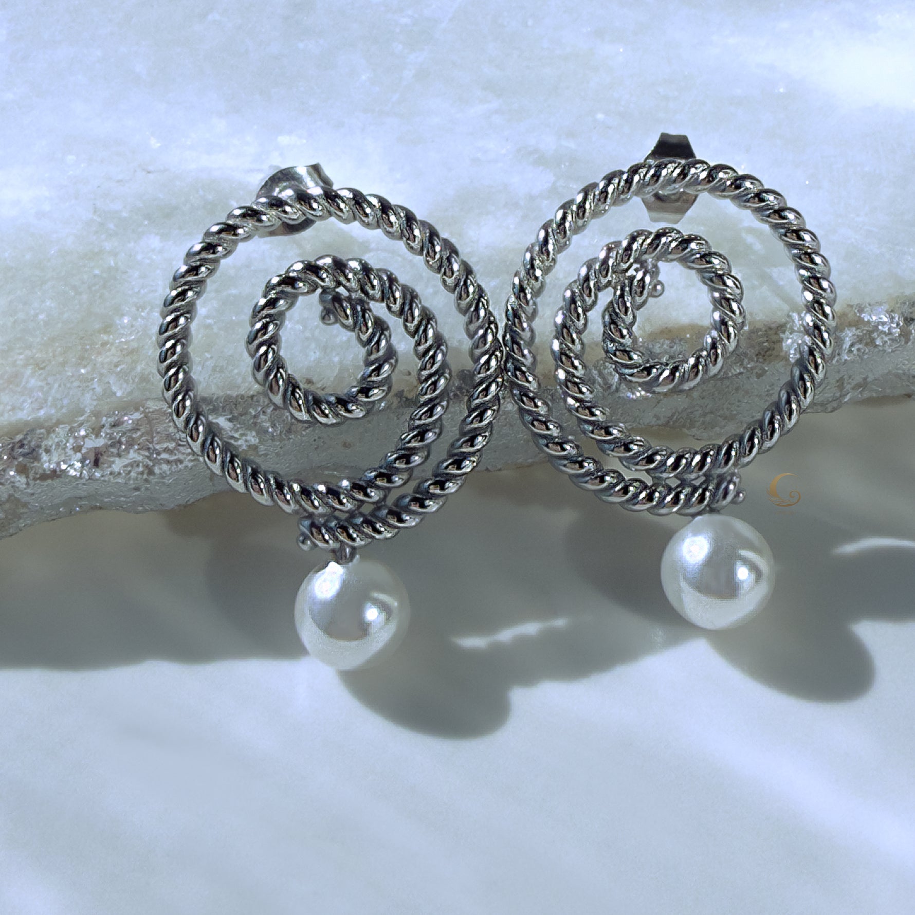 Thaleia silver spiral earrings with pearl-like drops on icy crystal surface