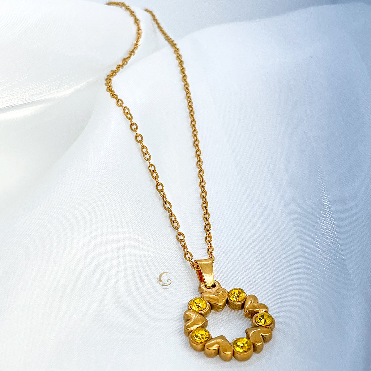 Full view of Solara gold necklace with round crystal heart pendant on white fabric