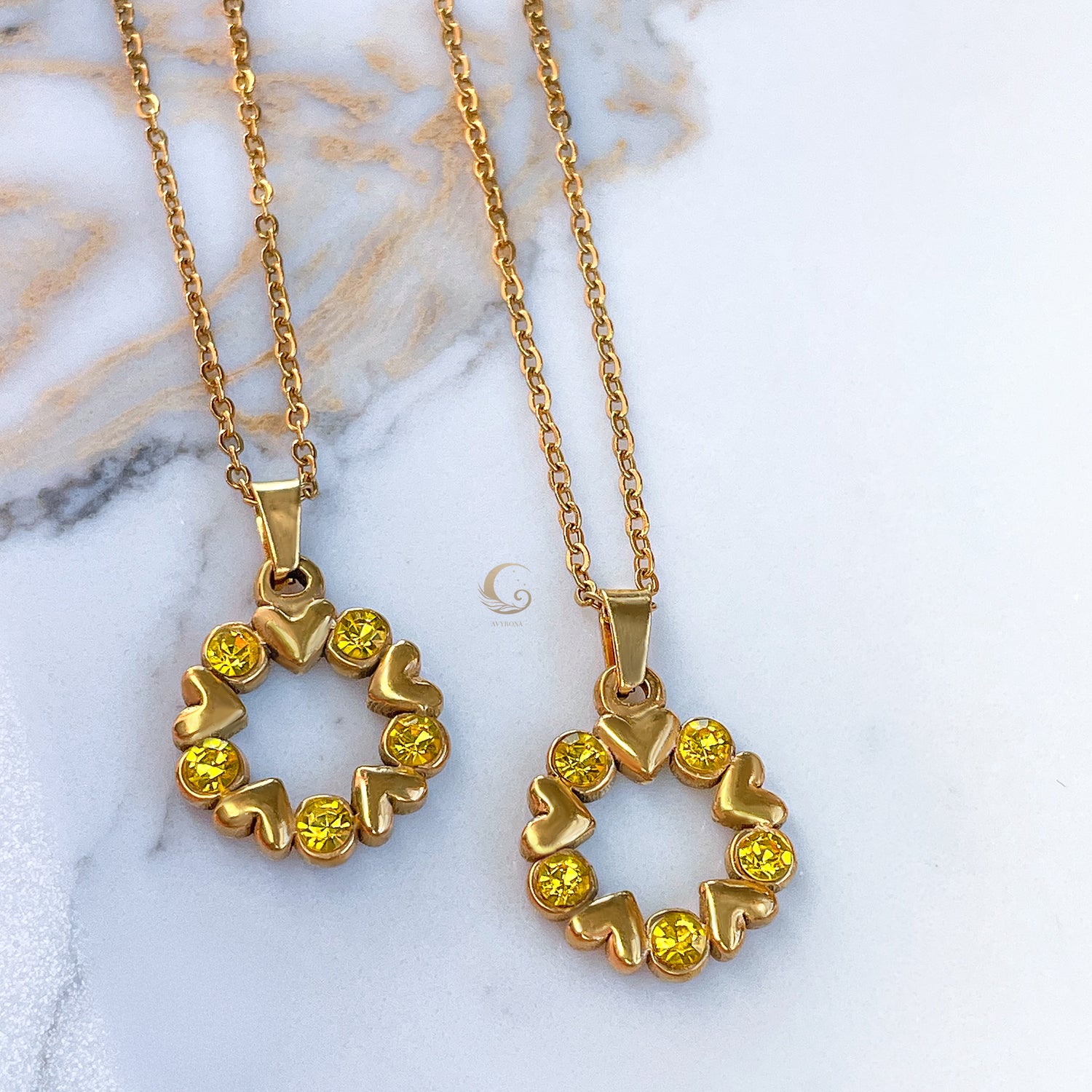 Gold heart and crystal wreath necklace, two pendants side by side on marble background, yellow stones glowing