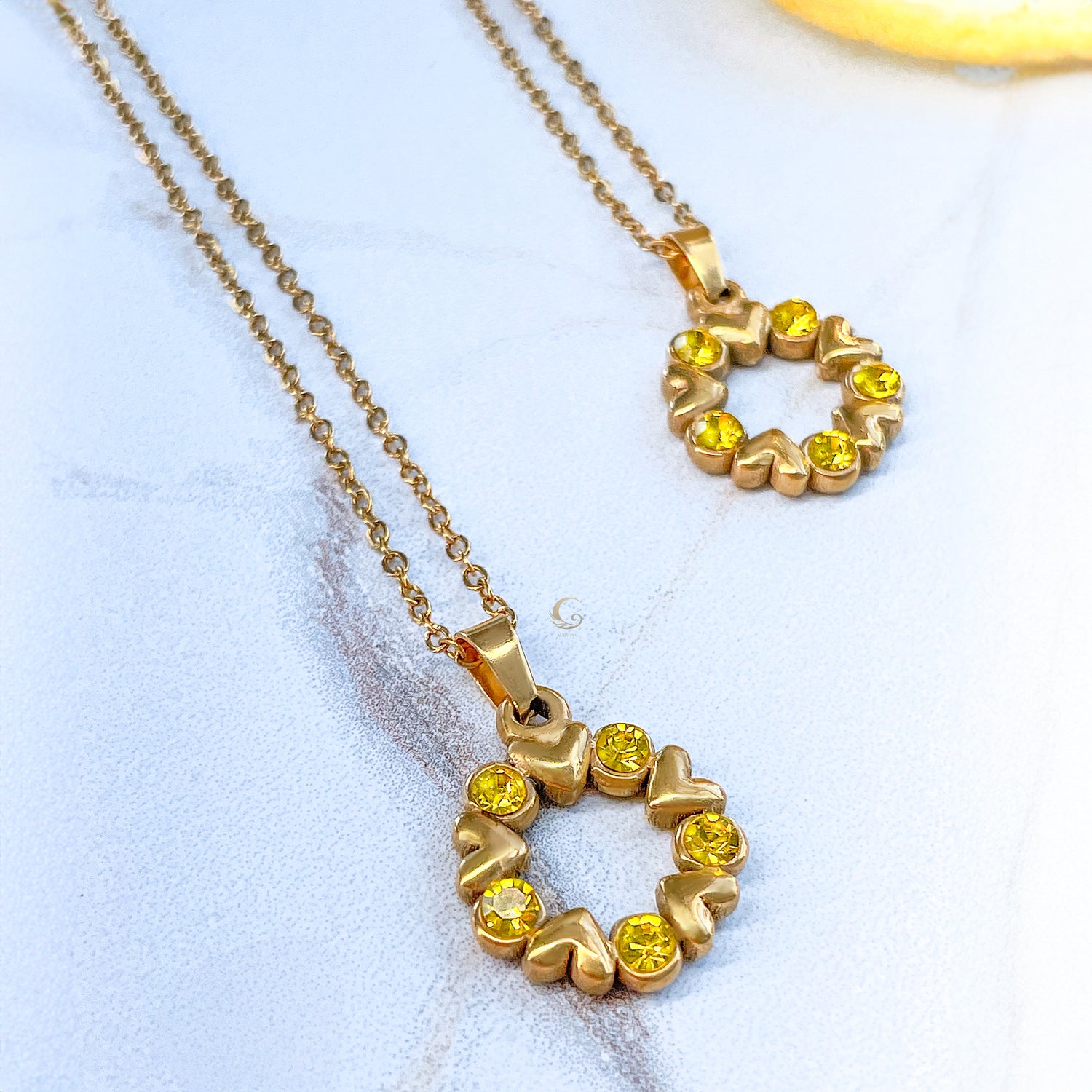 Pair of golden heart necklaces with yellow crystals on soft stone background, delicate and symbolic jewelry