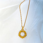 Close-up of Solara necklace pendant, golden hearts and yellow stones forming a circle, laying on light background