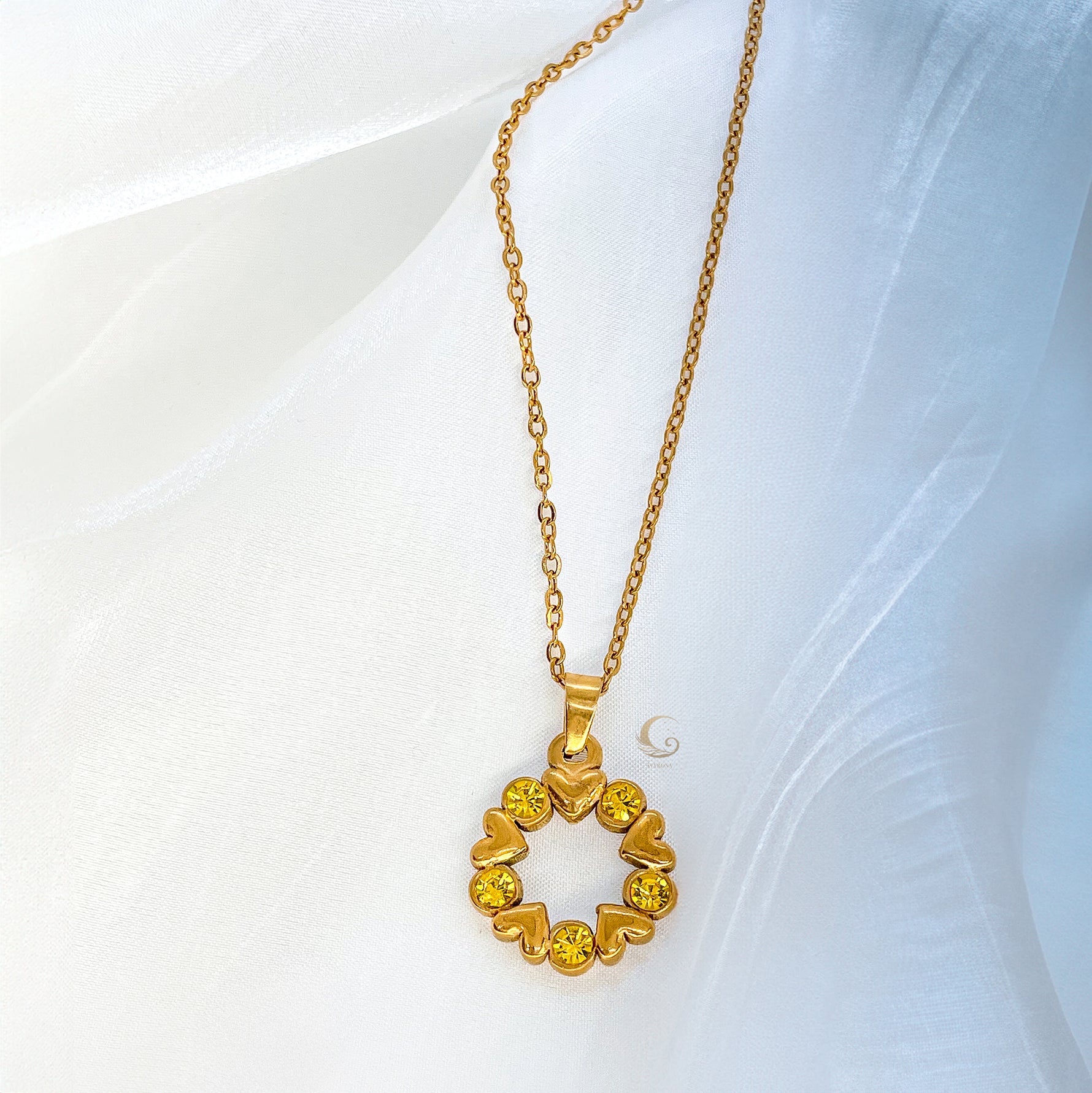 Close-up of Solara necklace pendant, golden hearts and yellow stones forming a circle, laying on light background