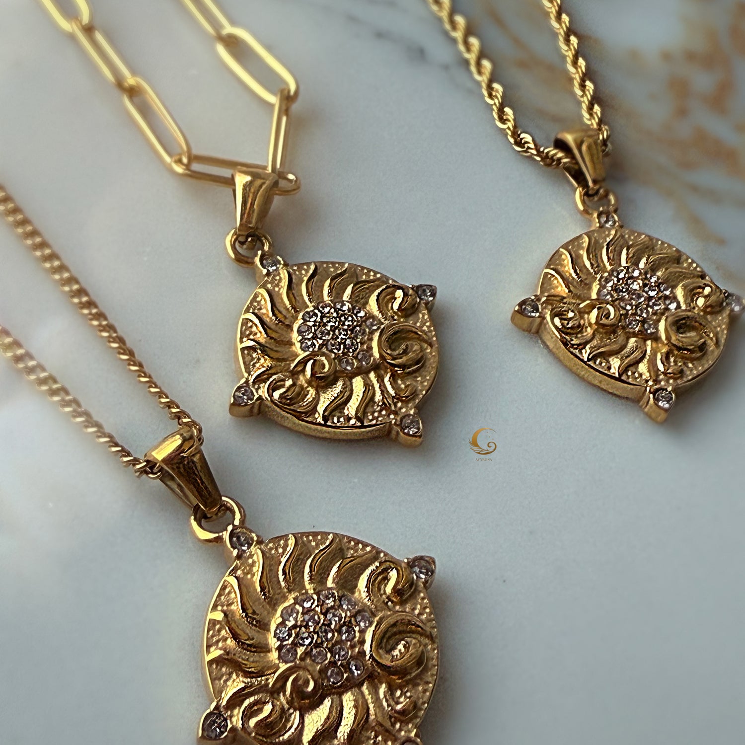 Three golden sun necklaces with different chain styles (paperclip, twisted, basic) displayed on marble — radiant and celestial