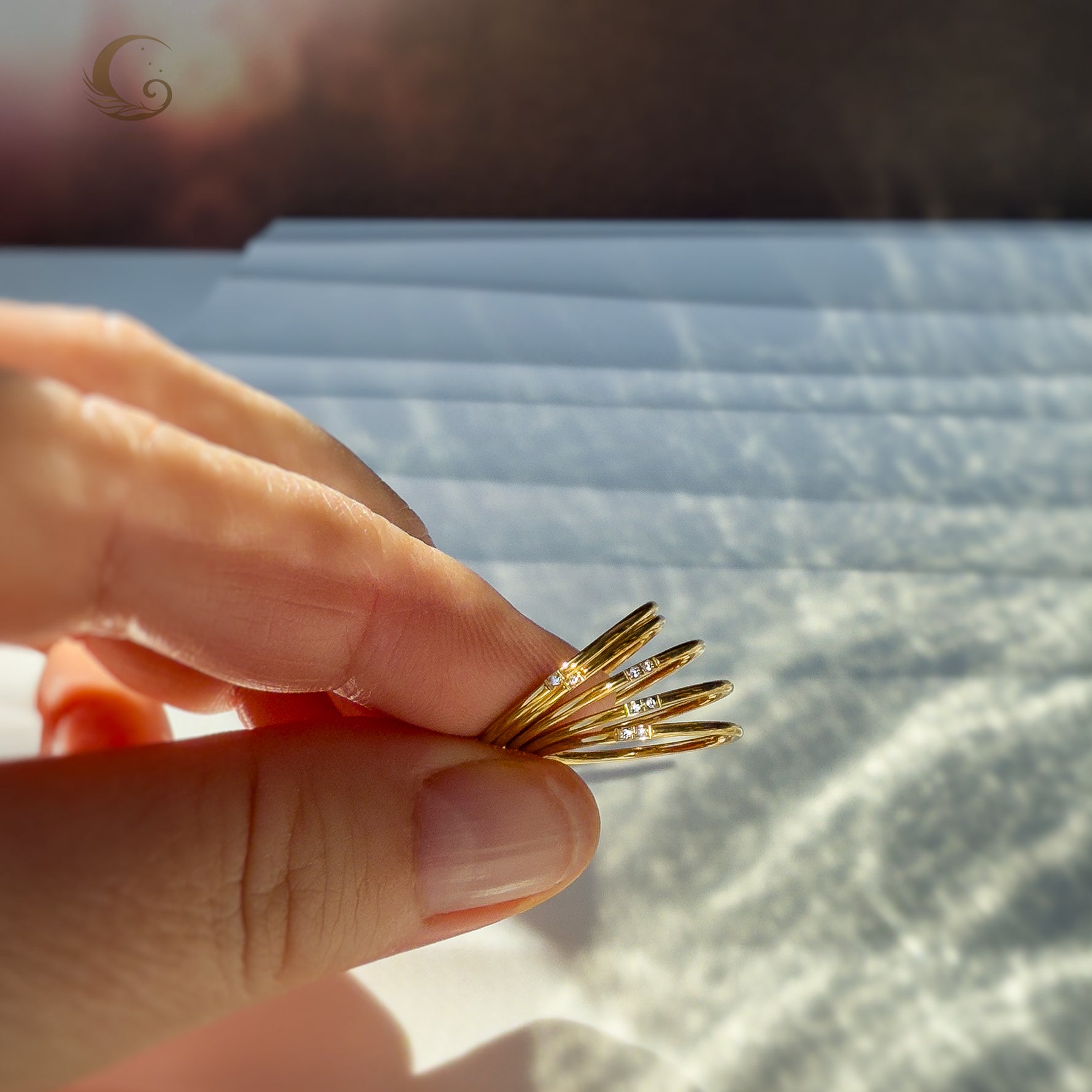Hand holding multiple thin gold rings with zircons, shown in soft light