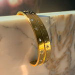 Close-up of two gold stainless steel bracelets with engraved stars and sparkling stones, styled on marble.