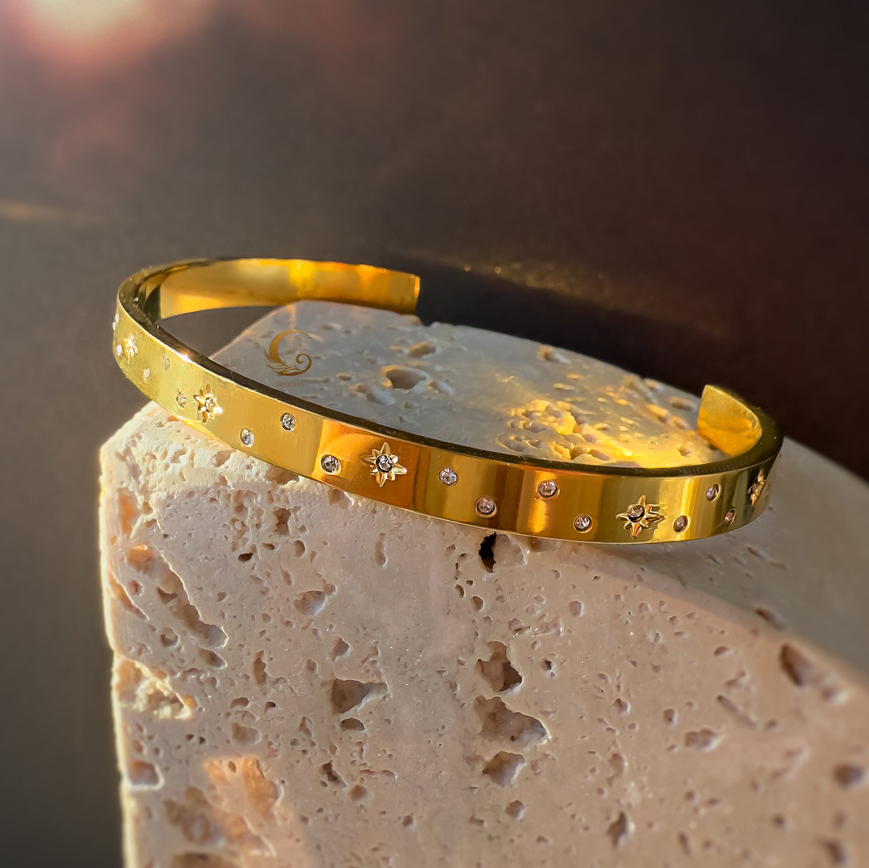 Celestial gold cuff bracelet with cubic zirconia and star engravings, placed on textured beige stone.