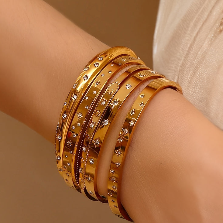 Stack of golden cuff bracelets with various starry patterns worn on wrist for a layered, celestial look.