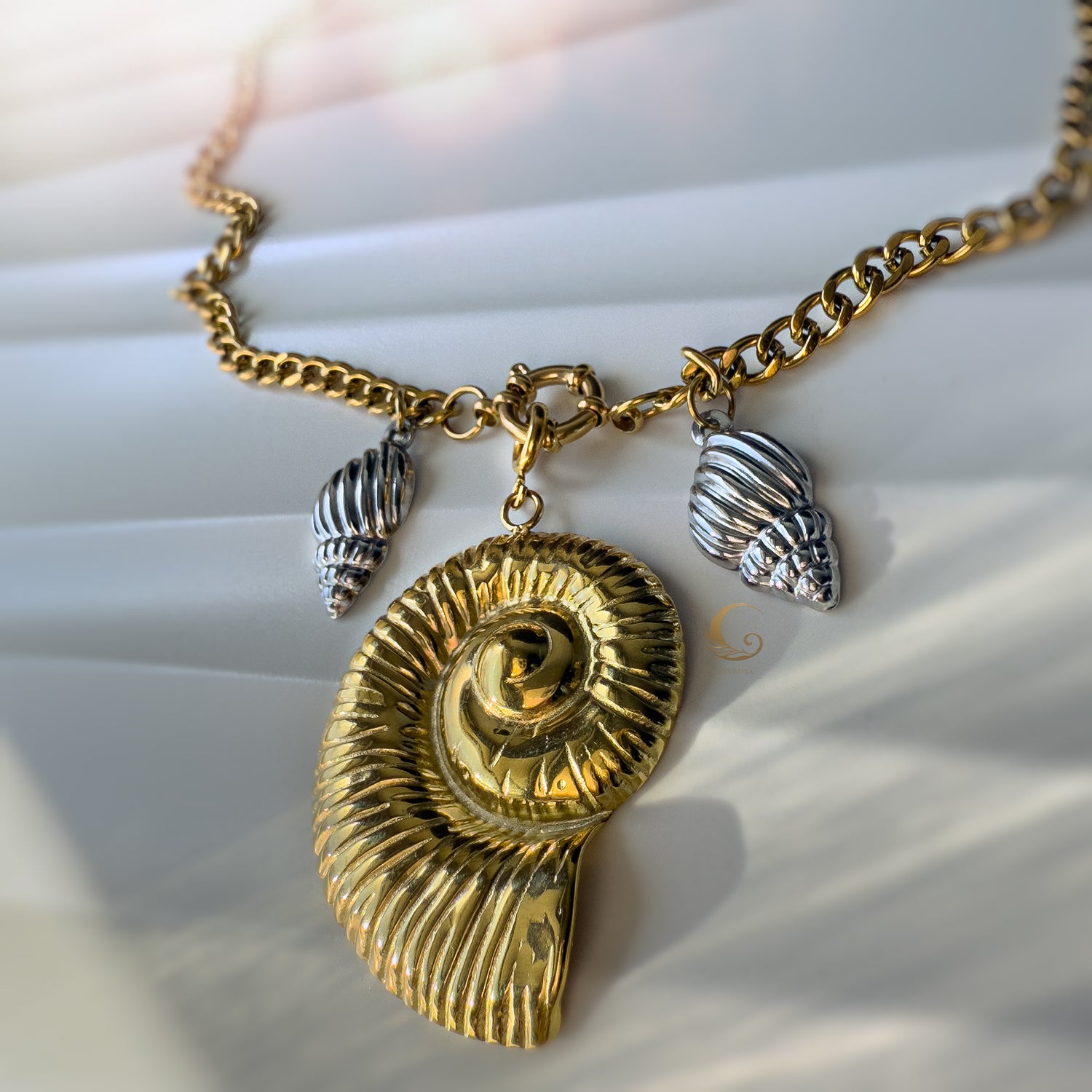 Front view of the Thalassa necklace highlighting the bold gold spiral shell and detailed silver charms, captured in soft natural light.