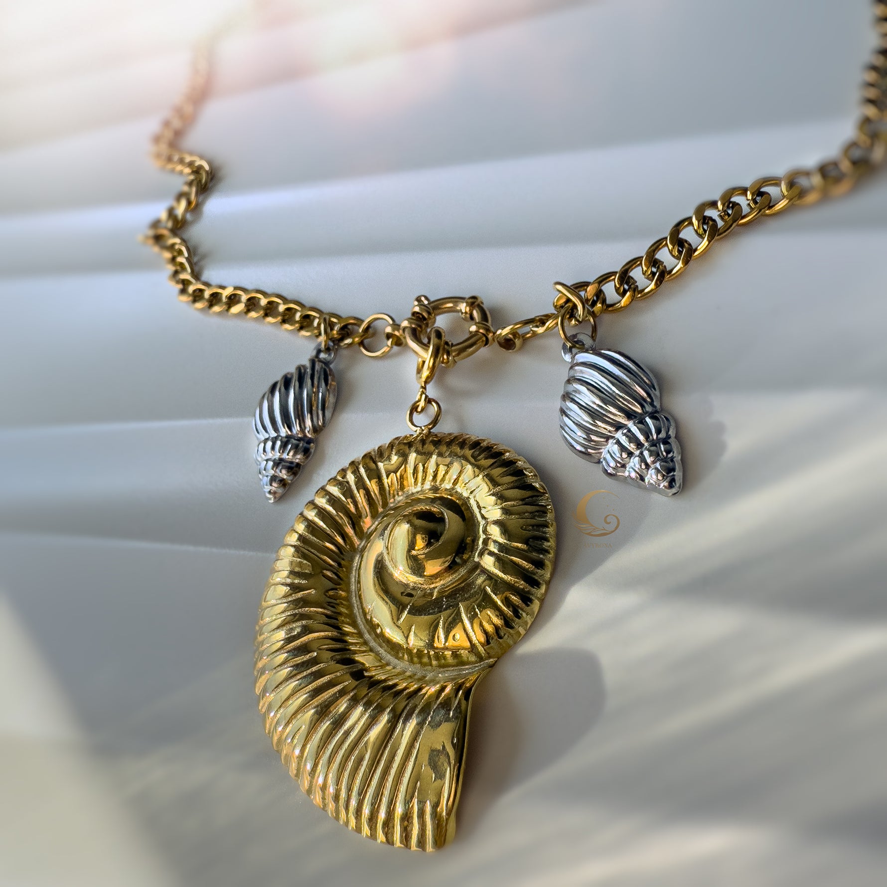 Front view of the Thalassa necklace highlighting the bold gold spiral shell and detailed silver charms, captured in soft natural light.