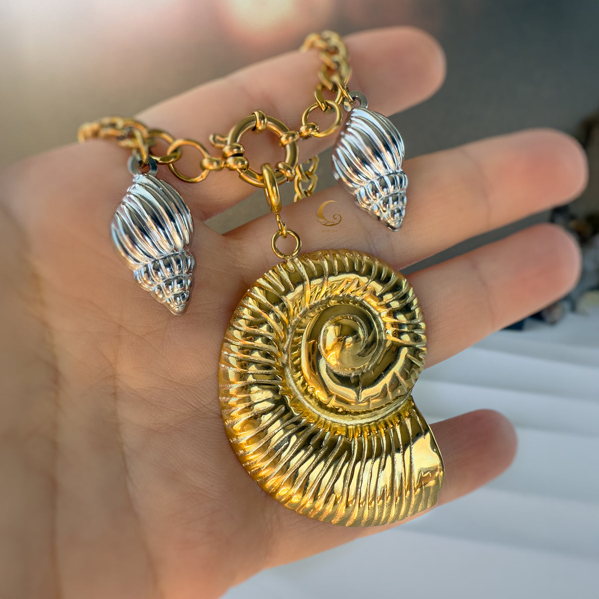 Hand-holding detail shot of the Thalassa necklace, showing scale and shine of the gold and silver shells.