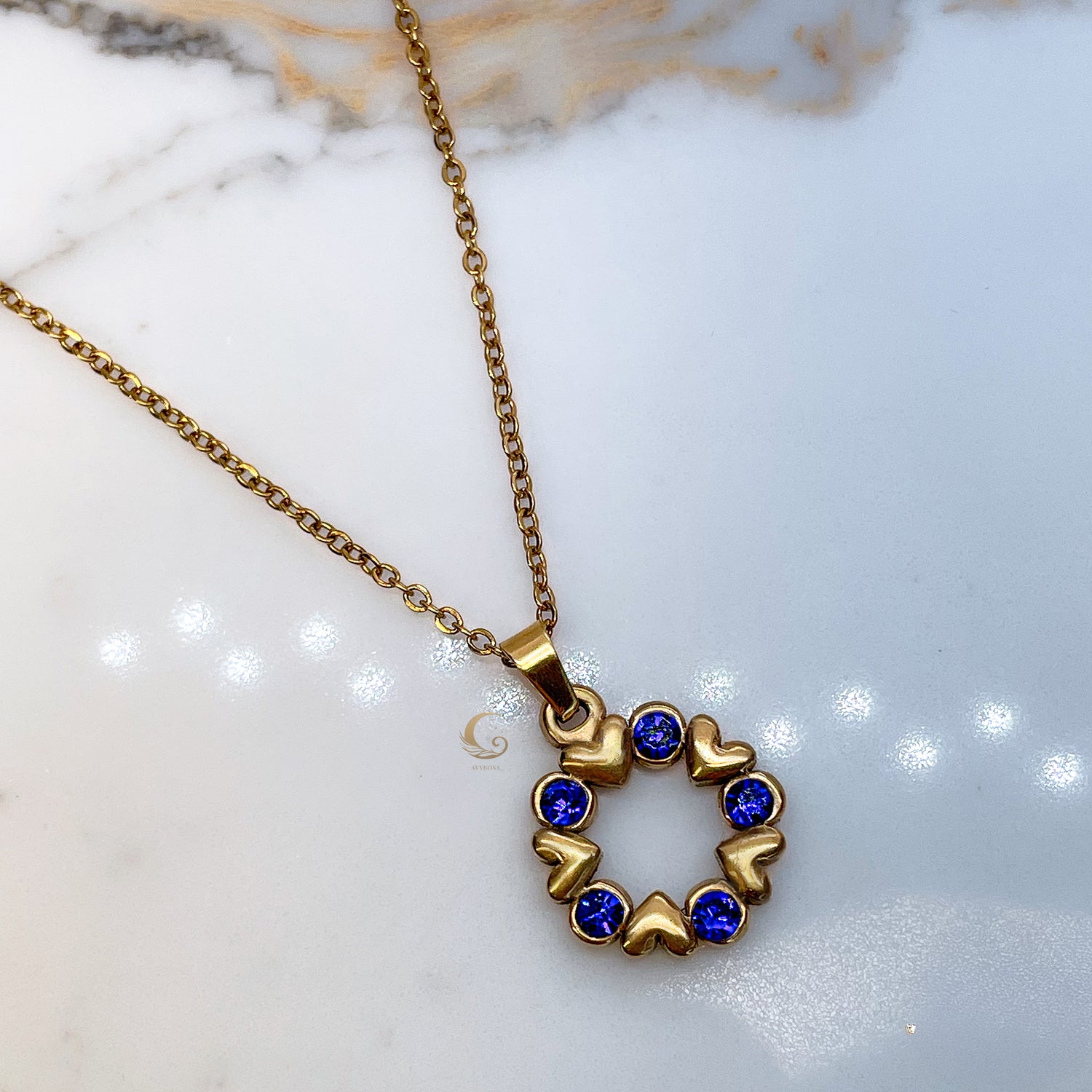 Single Vega necklace on marble surface, showing round pendant with deep blue crystals and golden heart frame