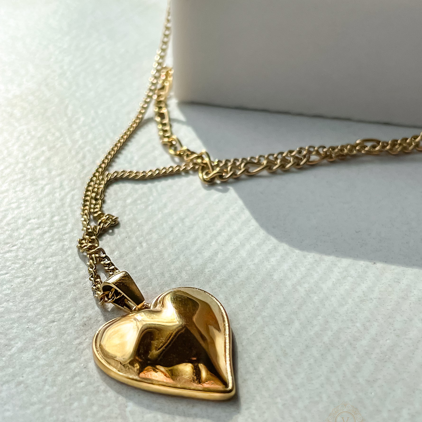 Layered gold necklace with heart pendant resting on white jewelry cloth, highlighting chain contrast and pendant shine.