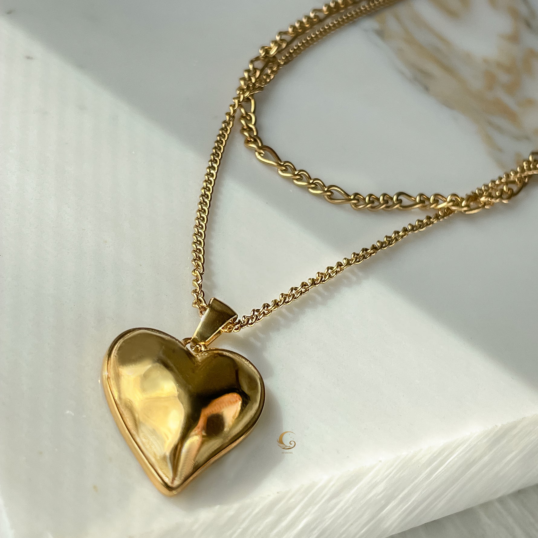 Gold layered heart necklace with double chains displayed on marble background in warm sunlight, showing vintage sculptural pendant.