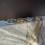 Set of four Wave rings on marble – two in polished silver and two in glossy gold finish, arranged in a soft light.