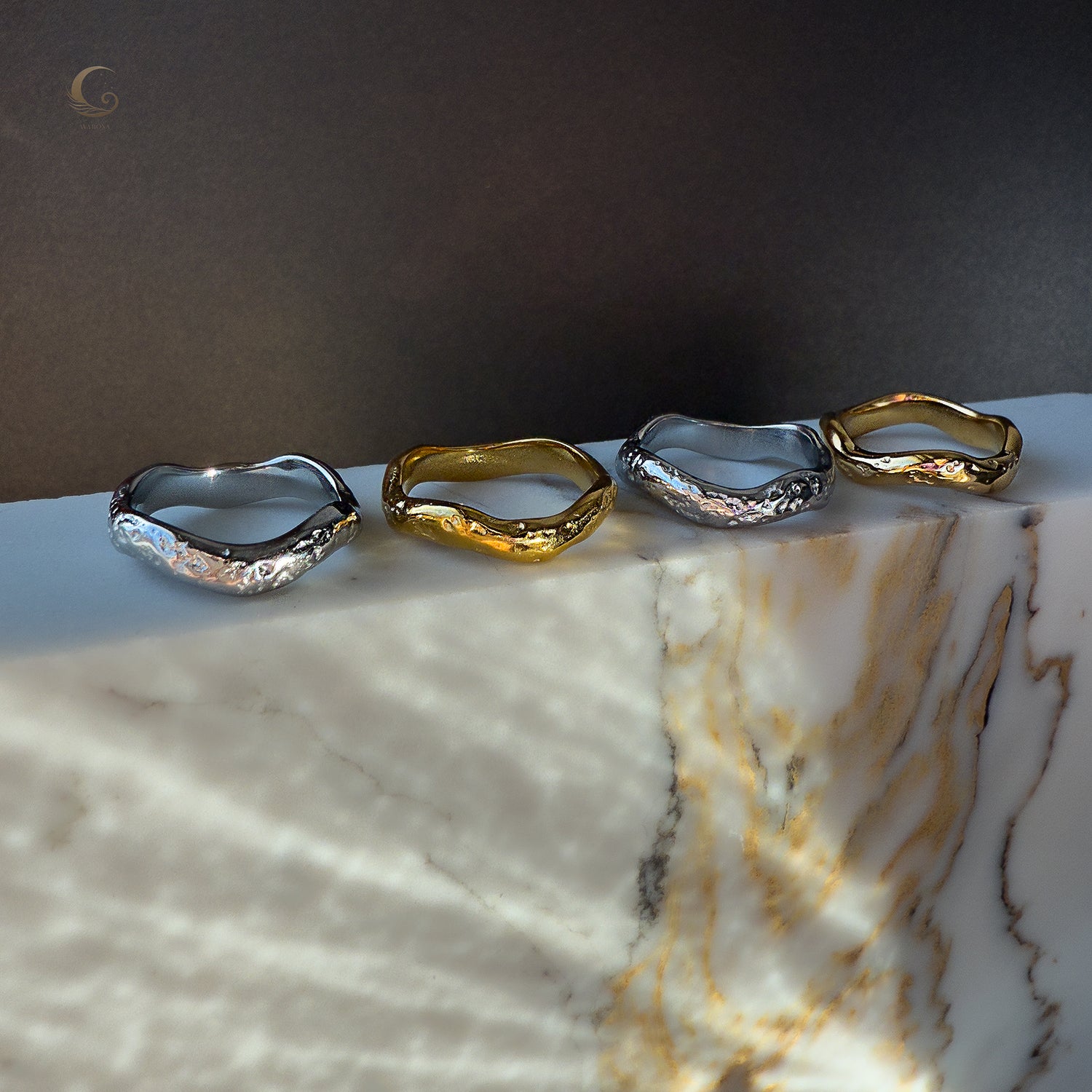 Set of four Wave rings on marble – two in polished silver and two in glossy gold finish, arranged in a soft light.