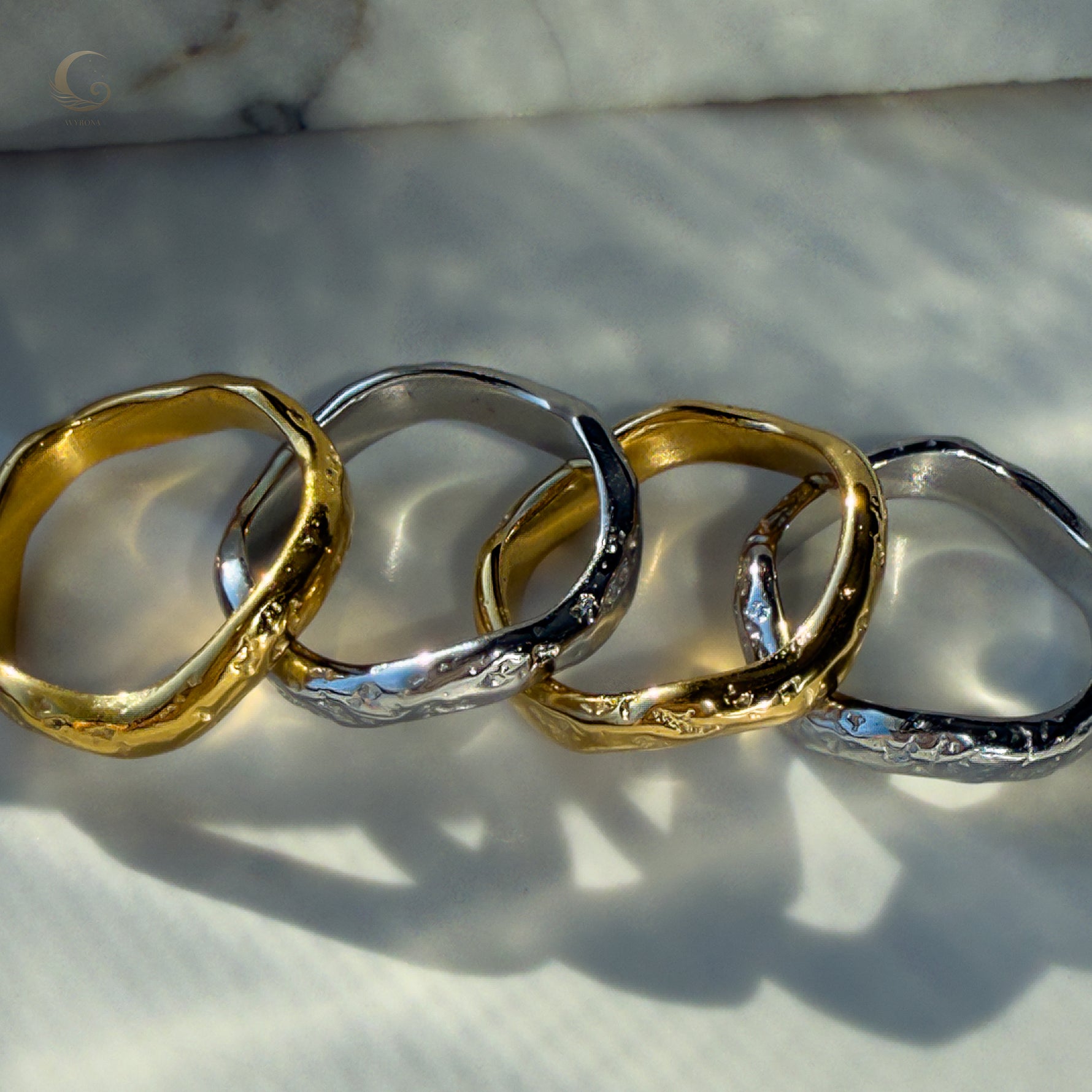  Artistic shot of four Wave rings in silver and gold tones, styled together with soft reflections.