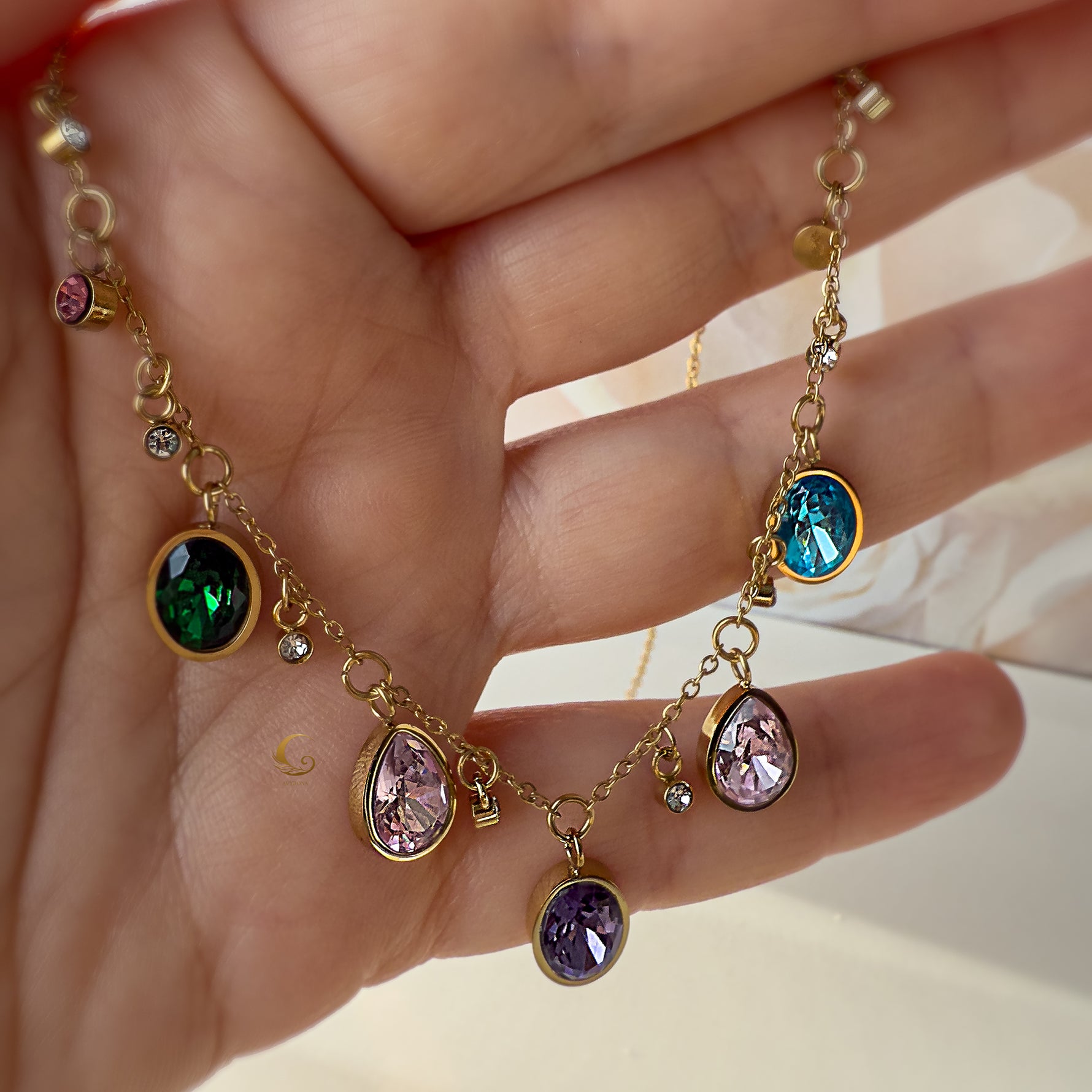 Close-up of Zaria charm necklace held in hand, showcasing crystal details